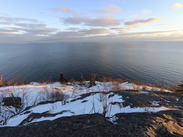 snowy, rocky cliff overlooking large body of water