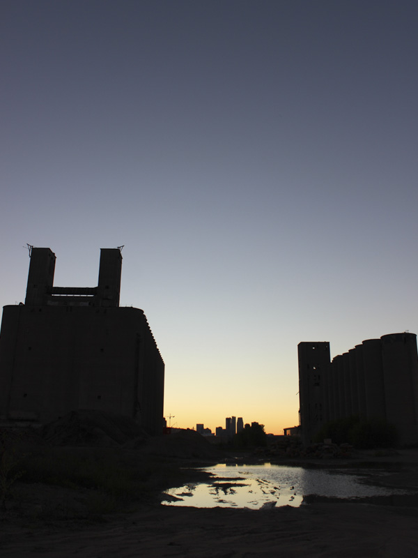 industrial buildings silhouetted against sunset with city in-between